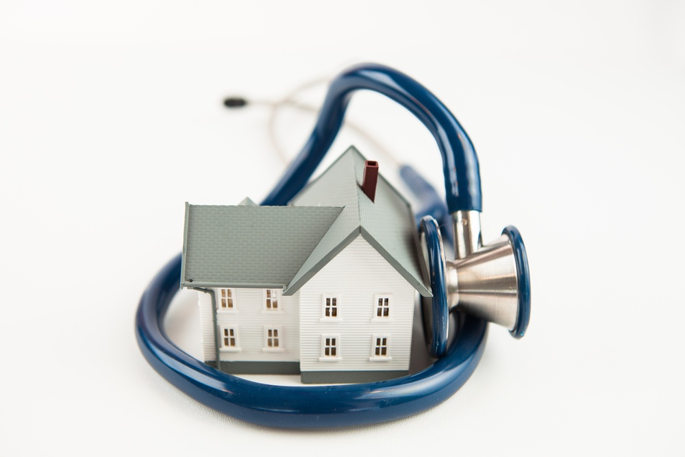 Blue stethoscope wrapped aroud tiny house model on white background
